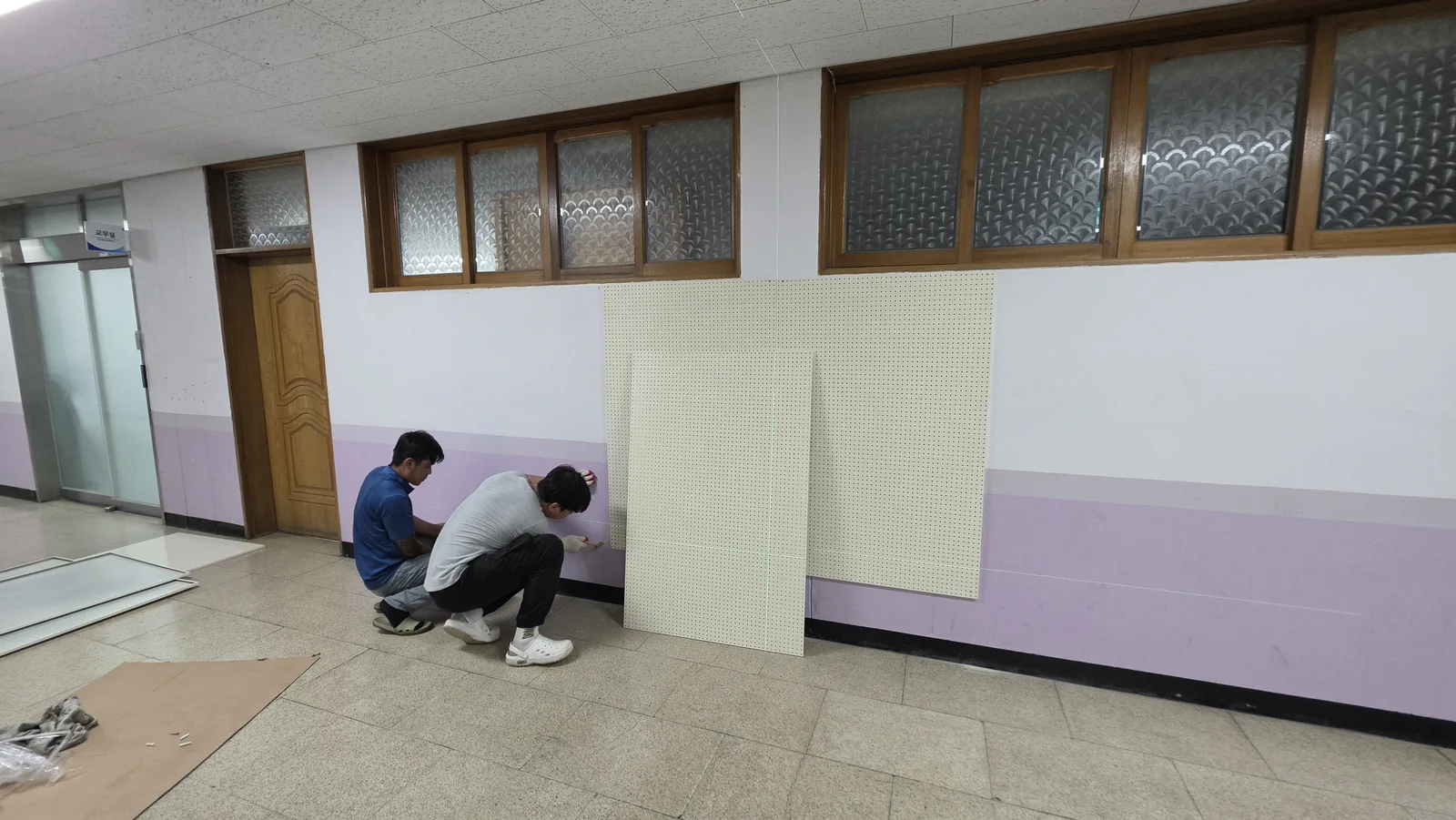 학교 복도에서 여러 장의 타공판을 벽면에 고정하는 시공 장면